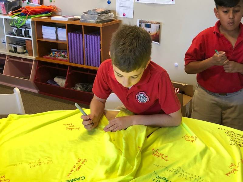 Children writing messages on a yellow banner.