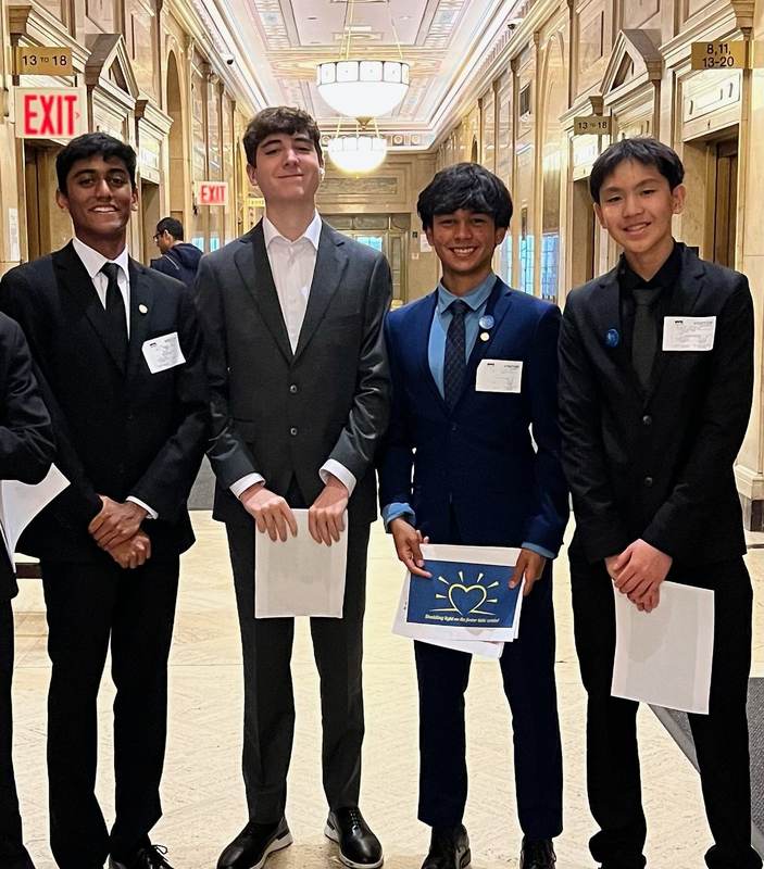 Three students holding a certificate in a Capitol hallway.